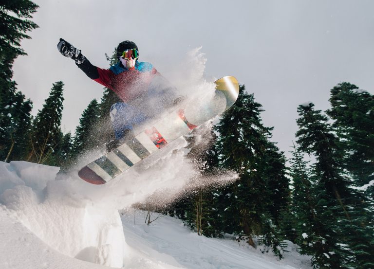 snowboarder is jumping very high and freeriding from hill in the mountain forest