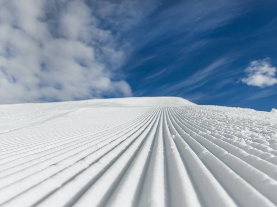 Close-up straight line rows of freshly prepared groomed ski slope piste with bright shining sun and